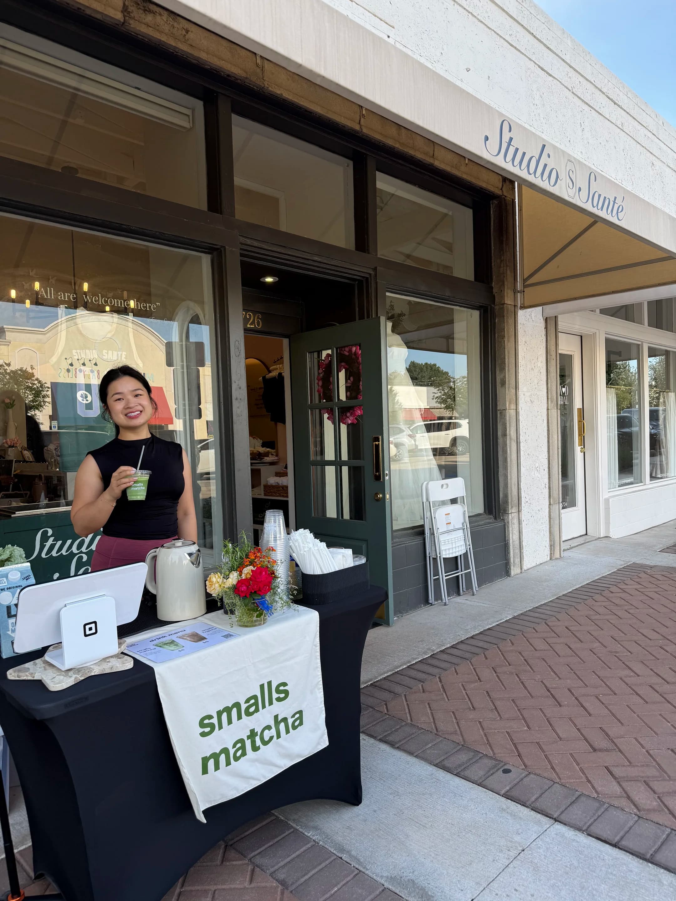 thy smiling behind a smalls matcha pop-up table outside studio santé